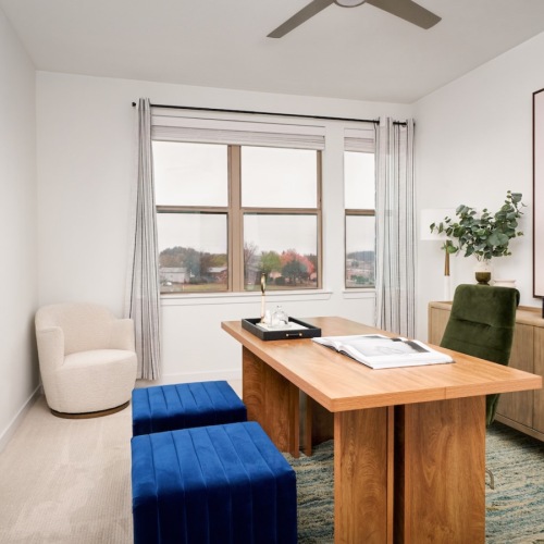 well lit office with window and a desk with a credenza and  a wall painting 